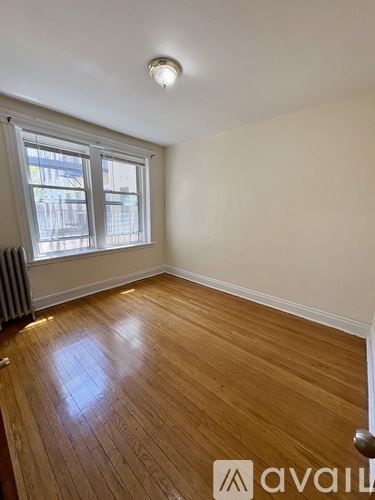 A room with wooden flooring and a window with a view of a building outside.
