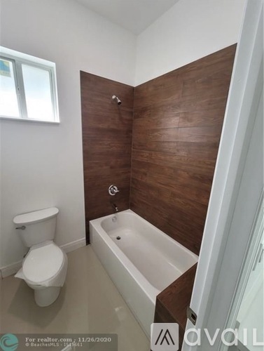 A white toilet sits in a bathroom with a wooden wall and a white bathtub.