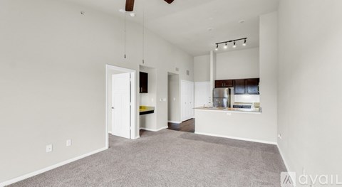 A spacious living room with a grey carpet and white walls.