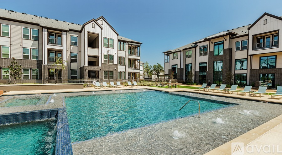 A swimming pool in front of apartment buildings with lounge chairs on the side.