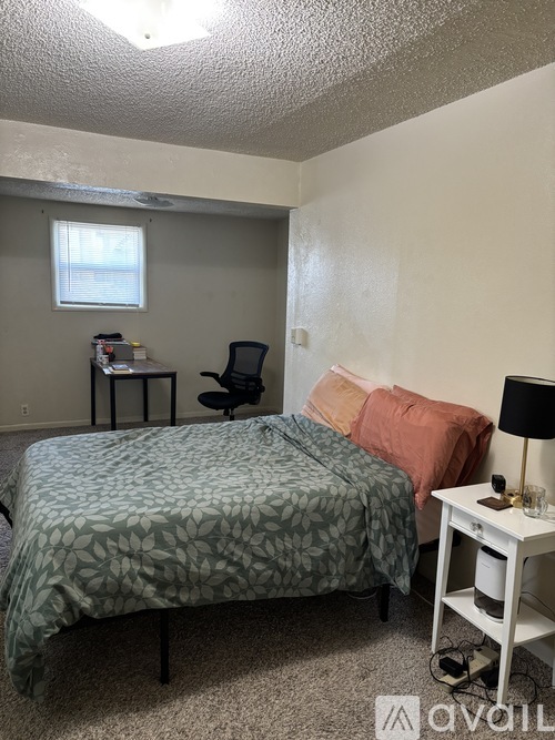 A bedroom with a bed, desk, chair, and window.
