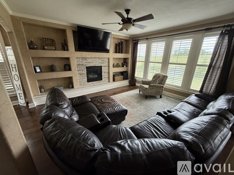 A living room with black leather furniture and a fireplace.