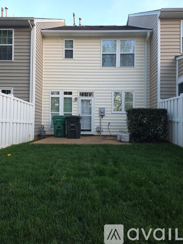 A house with a white fence and a green trash can in front.