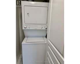A white dryer is in a small, white-walled laundry room.