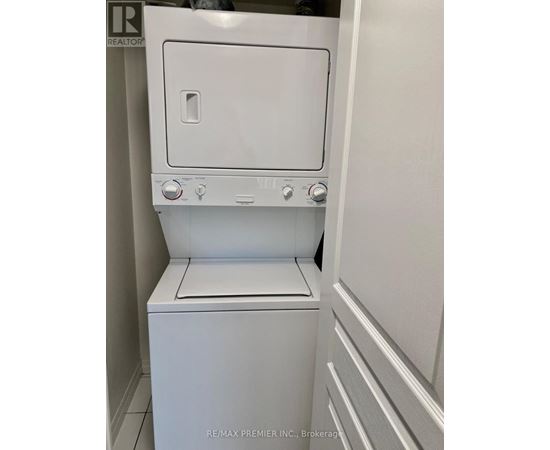 A white dryer is in a small, white-walled laundry room.