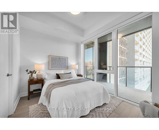 A bedroom with a large bed and a view of a building outside the window.