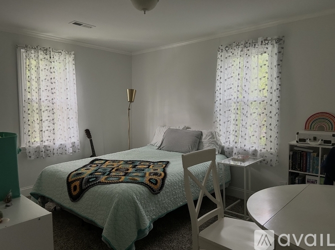 A bedroom with a bed, chair, and window with curtains.
