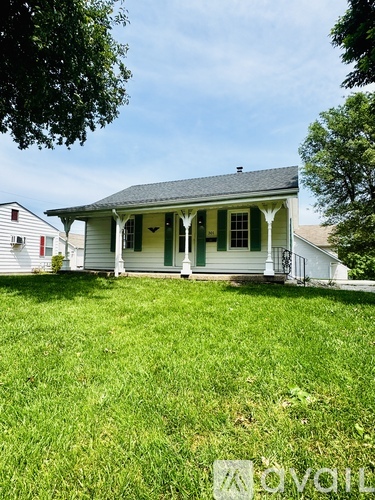 A white house with green shutters and a black roof.