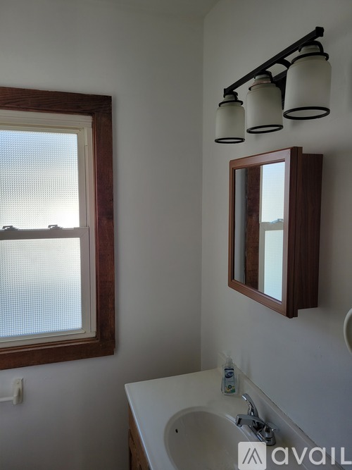 A bathroom with a white sink and a window with a wooden frame.