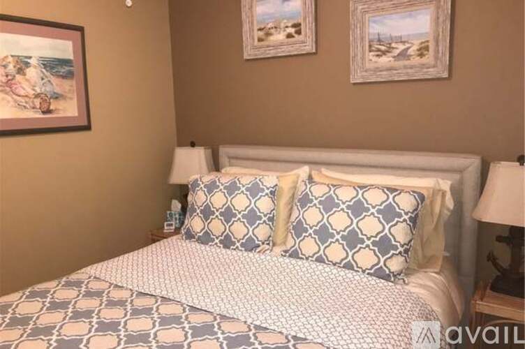 A bed with a white headboard and a patterned comforter is in the foreground with two framed pictures on the wall behind it.