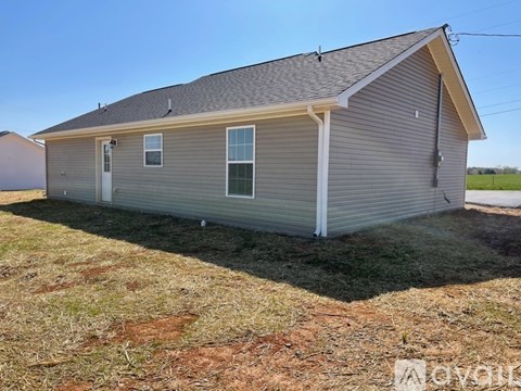 A small house with a grey roof and a white door is situated in a grassy area.