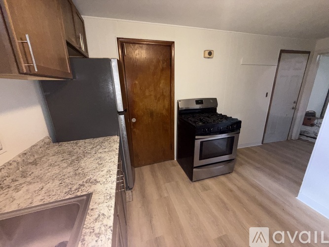 A kitchen with a black fridge, wooden door, and a stove top oven.