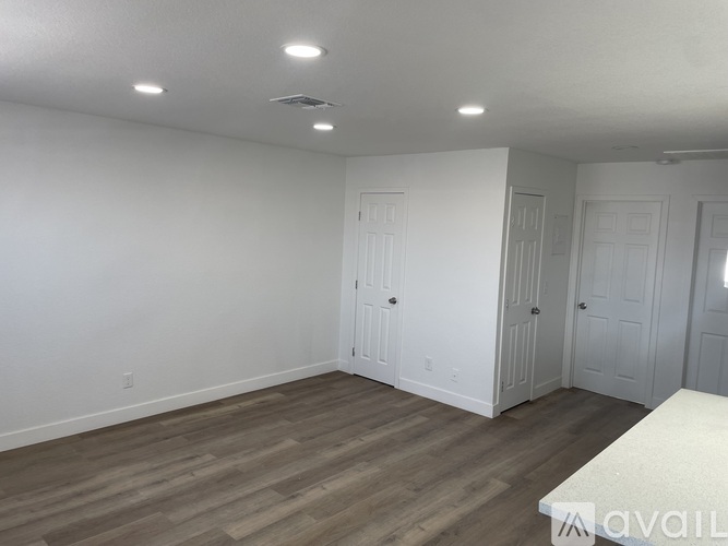 A room with white walls and wooden flooring, with a bed on the right side.