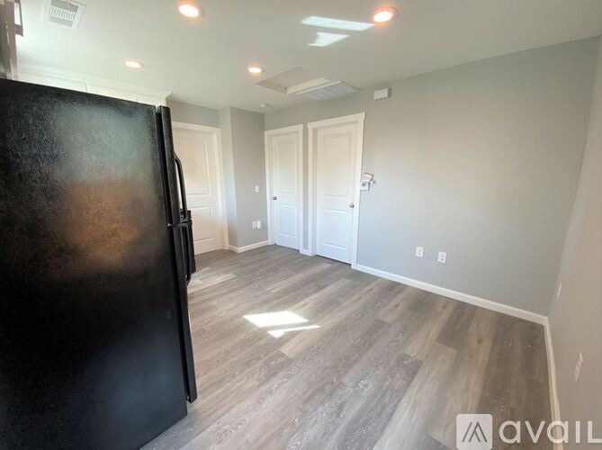 A black refrigerator is in the corner of a room with wood flooring and white walls.