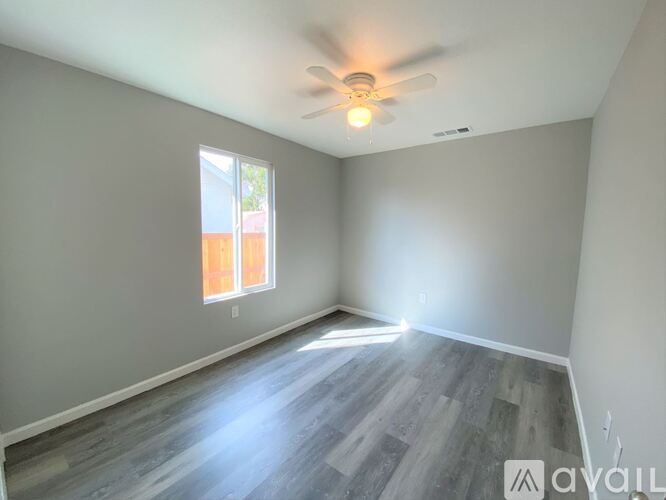 A room with a ceiling fan and a window with a view of a building outside.