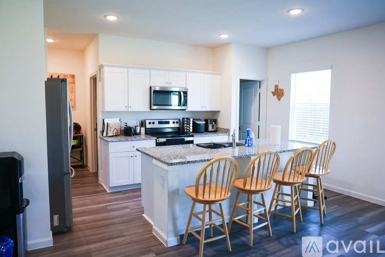 A kitchen with a refrigerator, microwave, oven, and a counter with four chairs.