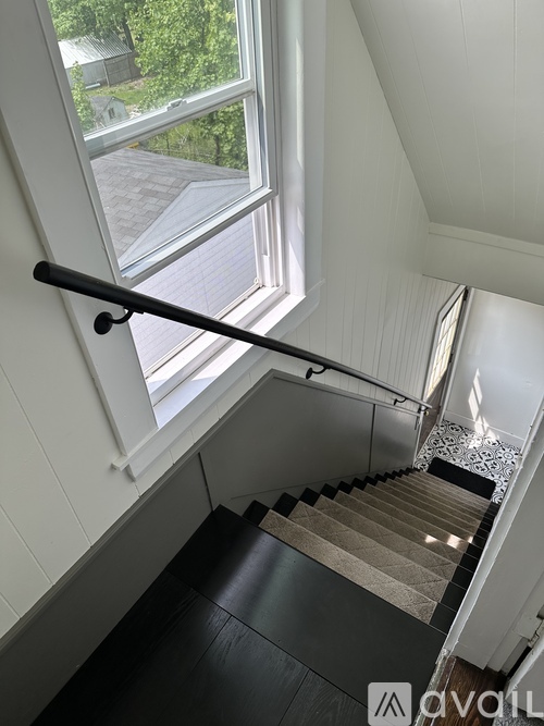 A staircase with a black handrail and a window overlooking a green landscape.