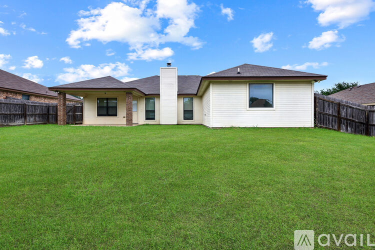 A house with a white exterior and a brown roof is surrounded by a green lawn.