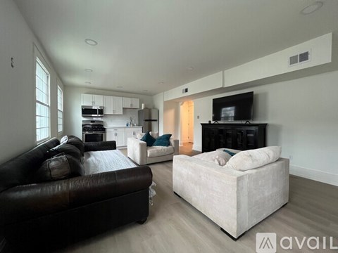 A living room with a black leather couch and a white couch with a television on the wall.
