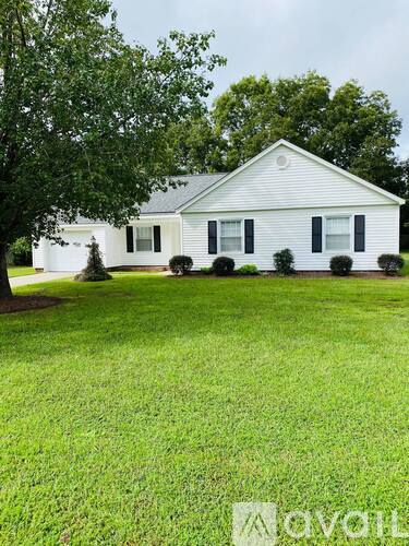 A white house with black shutters sits in a grassy yard.