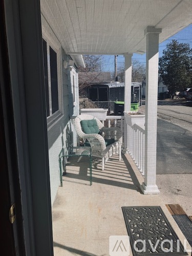 A white porch with a green chair and a black door.