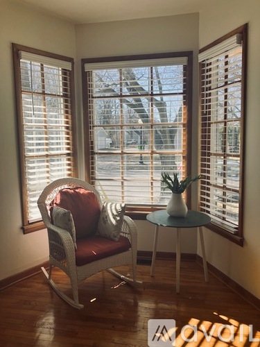 A chair with a red cushion is placed in front of a window with wooden shutters.