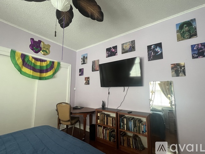 A bedroom with a bed, desk, chair, and a wall with pictures and a television.