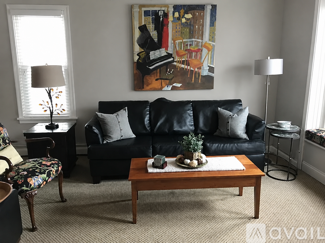 A living room with a black couch, a coffee table, and a painting on the wall.