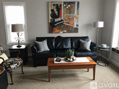 A living room with a black couch, a coffee table, and a painting on the wall.