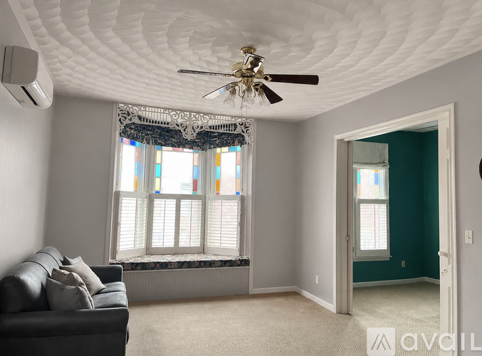 A living room with a couch, a ceiling fan, and a window with curtains.
