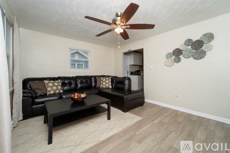 A living room with a black leather couch and a ceiling fan.