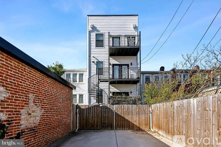 A white apartment building with a balcony and a wooden fence in front.