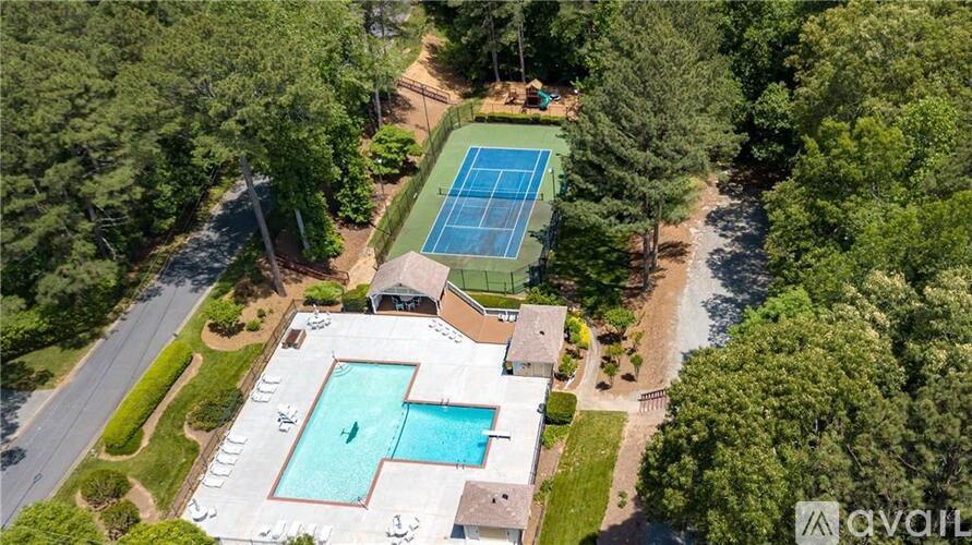 A tennis court is surrounded by trees and a pool is in the foreground.