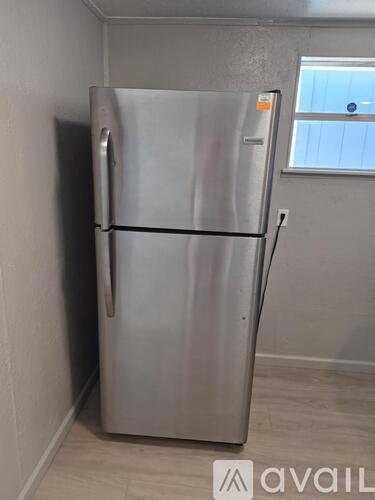 A silver fridge in a room with a window.