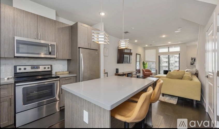 A modern kitchen with a stainless steel oven and microwave, a white island with chairs, and a living area with a couch.