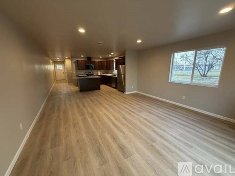 A spacious room with wooden flooring and a kitchen area in the background.