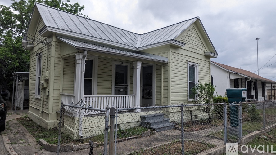 A small house with a porch and a fence in front.