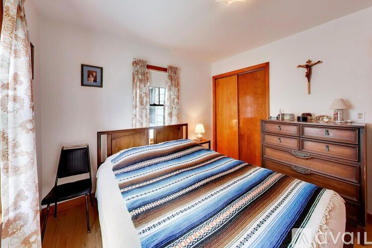 A bedroom with a bed, a chair, a dresser, and a cross on the wall.