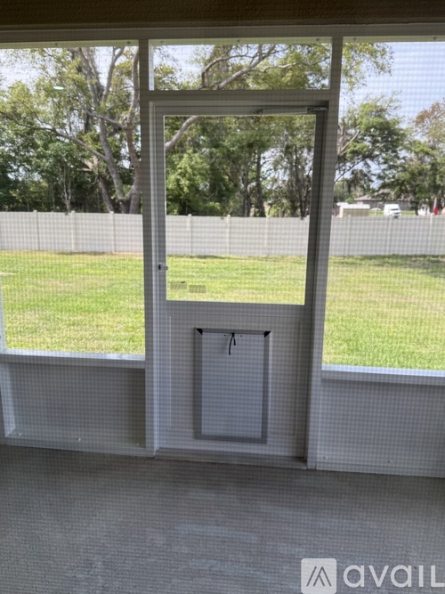 A window with a view of a green field and trees.