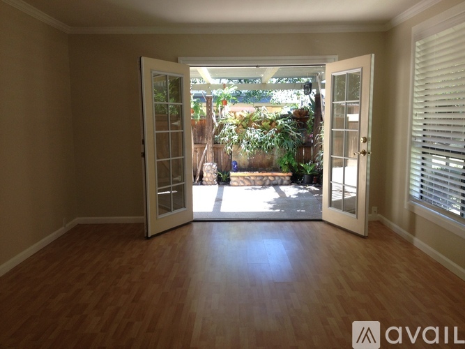 A room with wooden floors and a view of a garden through the open door.