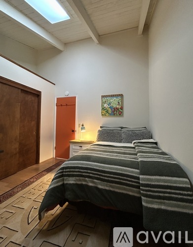 A bedroom with a bed, a painting on the wall, and a patterned rug on the floor.