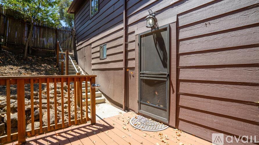 A wooden deck leads to a house with a closed door and a window.