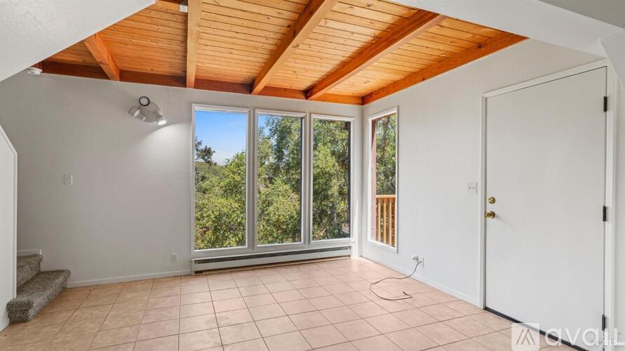 A room with a wooden ceiling and a large window with a view of trees.