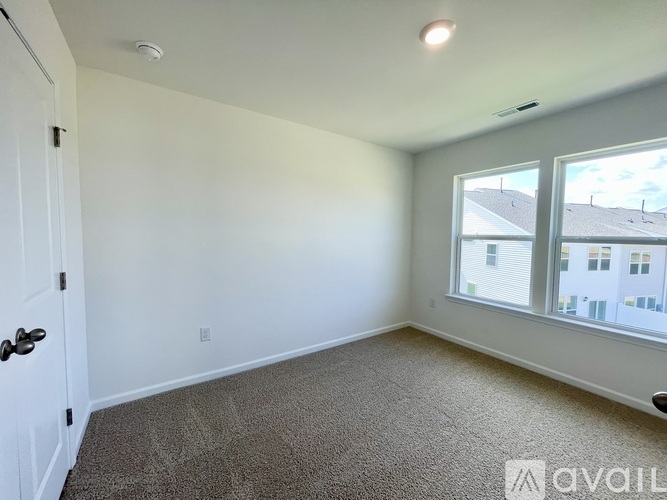 A room with a carpeted floor, a door, and a window showing a view of other buildings.