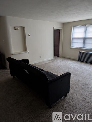 A black couch sits in a living room with a window and a door in the background.