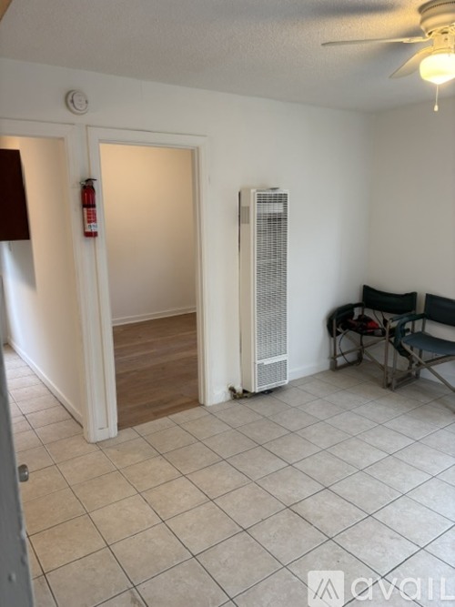 A room with a white tile floor, a white wall, a white door, a white ceiling fan, a white air conditioning unit, and a black chair.