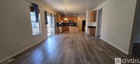 A spacious living room with wood flooring and a kitchen area in the background.