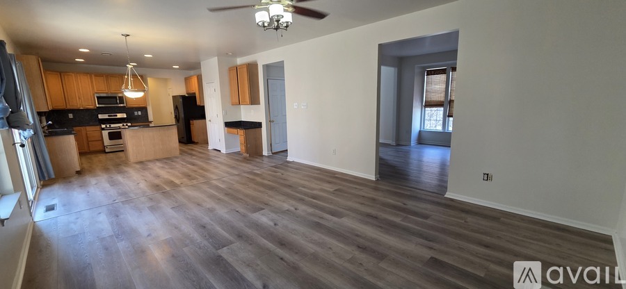 A spacious living room with a kitchen in the background and a ceiling fan above.