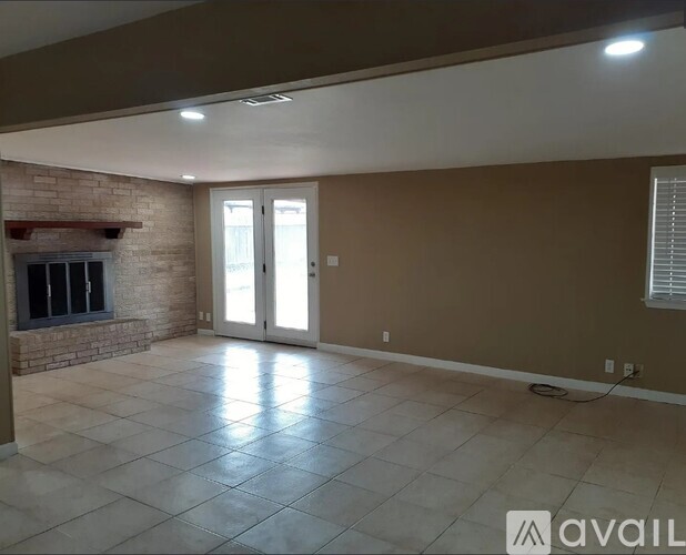 A spacious room with a brick fireplace and tiled flooring.
