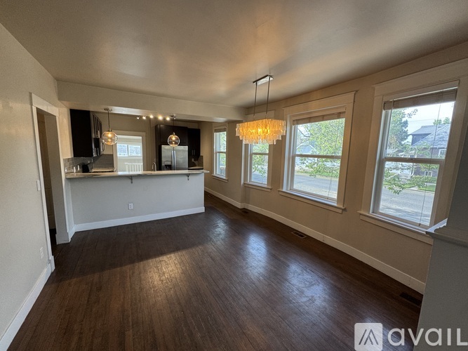 A spacious living room with hardwood floors and a kitchen area in the background.